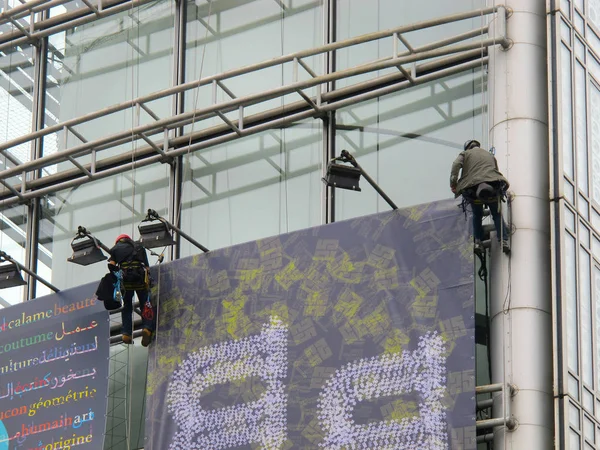 Workmen setting up a huge billboard on the facade of a modern building.