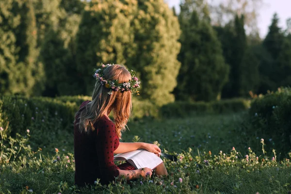 Attractive woman in wreath reading at nature, back