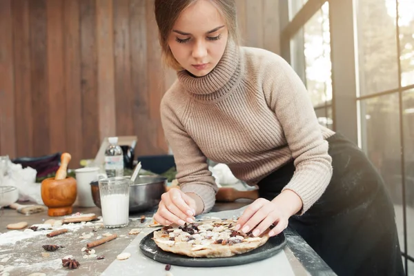 Woman decorating pie with dried fruits, free space