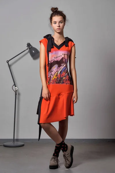 Pretty young fashion model in designers dress posing near metal floor lamp