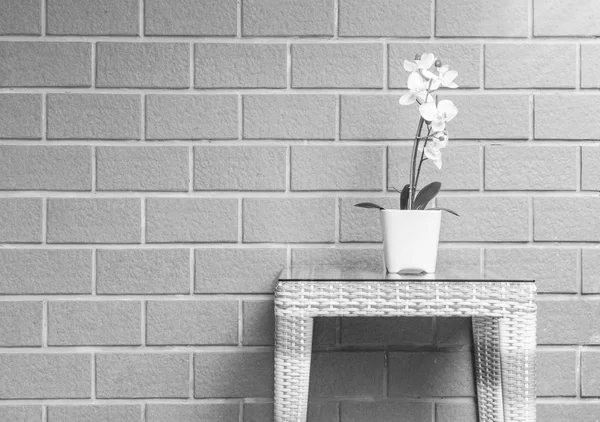 Closeup artificial plant with white orchid flower on flower pot on wood weave table on blurred brick wall texture background , beautiful interior in relaxation concept of house in black and white tone