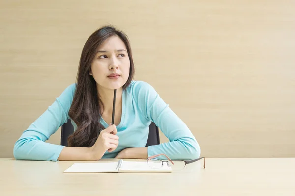 Closeup asian woman working with thinking face emotion and a pencil in her hand on blurred wood desk and wood wall textured background in the meeting room , woman with thinking concept