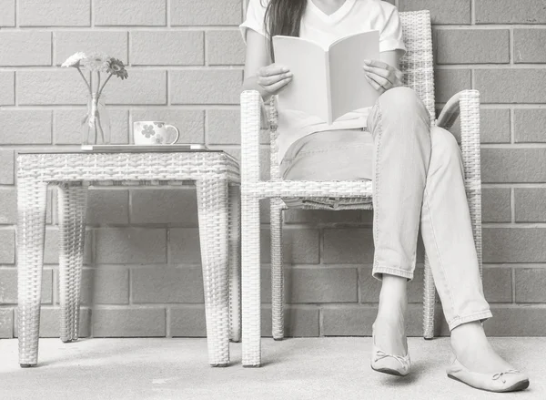 Woman sitting on wood weave chair in house for reading a white book in free time in the afternoon , relax time and lifestyle of asian woman concept in black and white tone