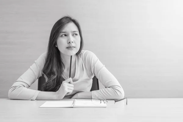 Closeup asian woman working with thinking face and a pencil in her hand on blurred wooden desk and wall textured background in the meeting room , woman with thinking concept in black and white tone