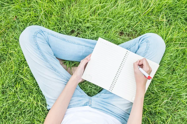Closeup asian woman sitting on grass field textured background for writing on note book under day light in the garden