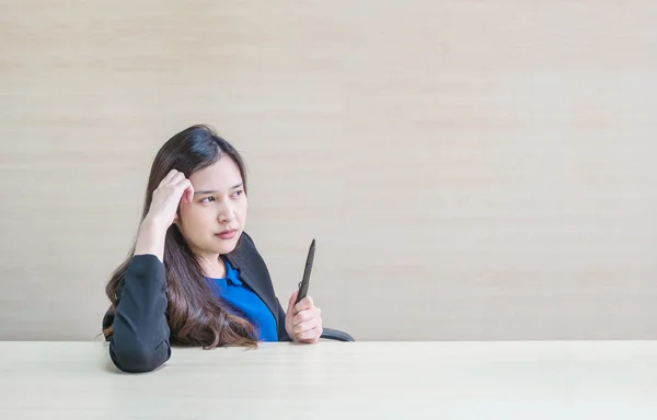 Closeup asian woman working with thinking face and a pen in her hand on blurred wooden desk and wall textured background in the meeting room , woman with thinking concept
