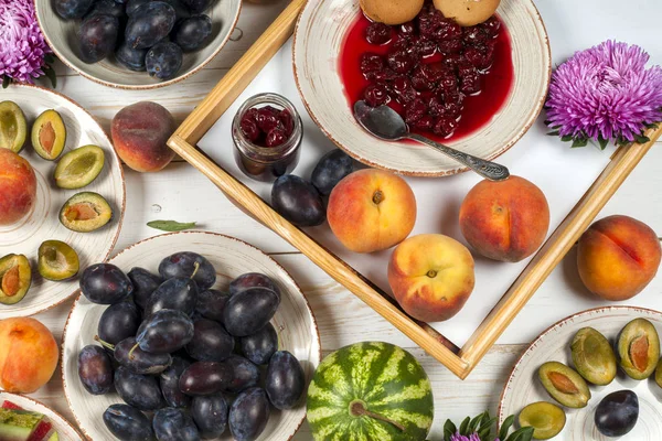 Colorful fruit set of purple, red and orange background in bowls. Plum, peaches, watermelon sliced above white tabletop