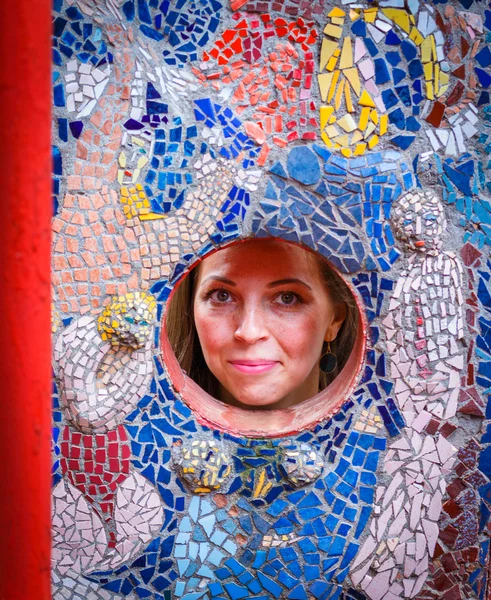 Womans face in a round hole in the mosaic wall.