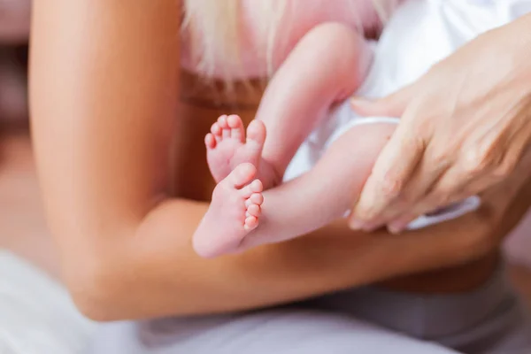 Mother holds newborn baby\'s bare heels. Tiny feet in woman\'s hand. Cozy morning at home.