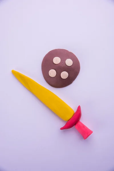Model of sword and shield made up of play dough or playdough or colourful clay, selective focus isolated over white background