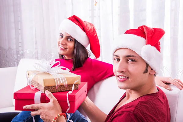 Merry Christmas. Young indian or asian couple celebrating Christmas at home with surprise gift boxes