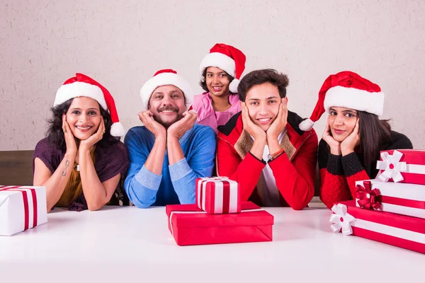 Christmas time, Happy indian family sitting across table with hands on chin with christmas gifts and santa hat/cap, merry Christmas, indian family celebrating christmas