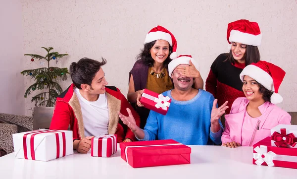Christmas time, Happy indian family sitting across table and exchanging christmas gifts wearing santa hat/cap, merry Christmas, indian family celebrating christmas