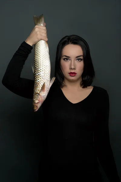 The woman holds live fish in hand