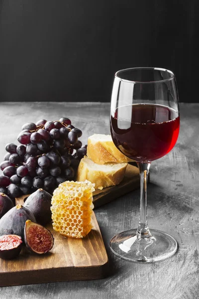 Red wine with fig, dark grapes, honey, bread on a dark backgroun
