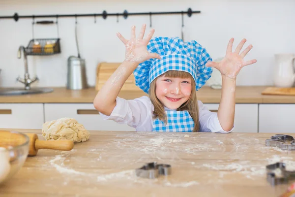 Portrait of pretty little girl in a cook clothes looks shows her fingers on a kitchen