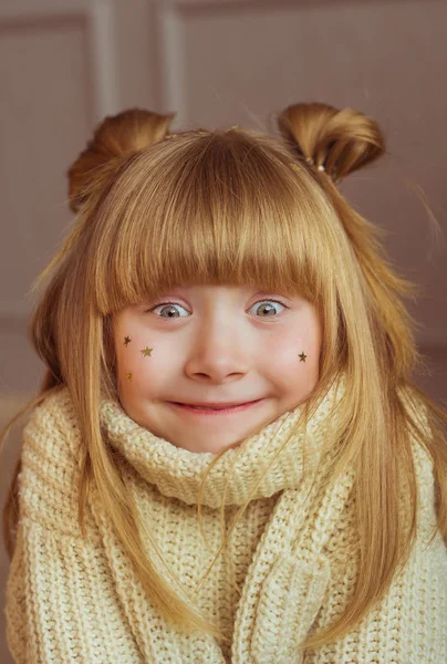 Portrait of a charming little girl in beige sweater makes faces at home