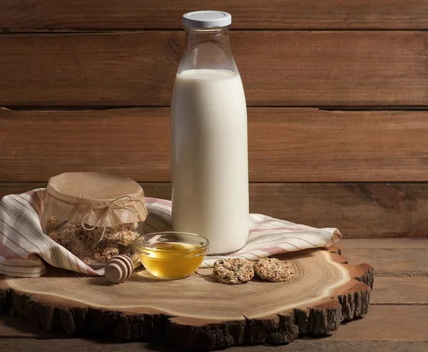 Bottle with milk, honey, cookies on round wooden plate and wooden background.