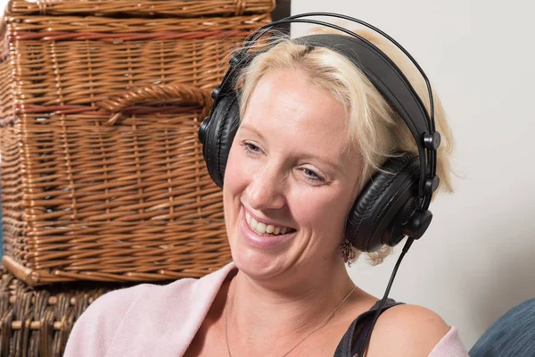 Sitting Blonde Woman in Headphones Tilts Head and Smiles