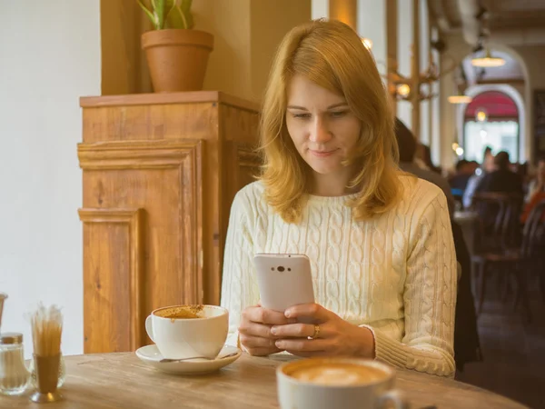 Attractive woman in a white sweater in a cafe looking at mobile