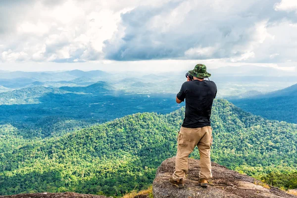 Male photographer enjoying and taking top view valley rain forest photo from mountain cliff.