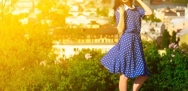 Young beautiful woman in a blue sundress posing in the summer against the backdrop of the city