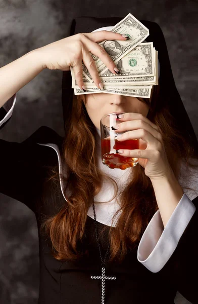 Close-up of attractive sexy nun with dark hair closes her eyes dollar bills and drinking alcohol