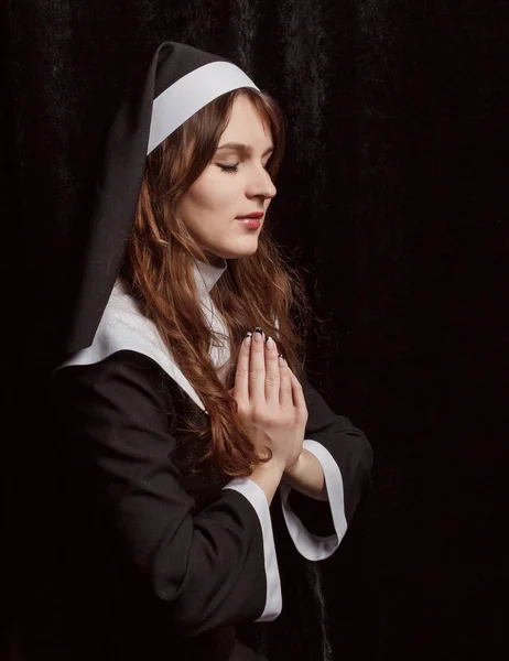 Nun sitting on his lap with her hands clasped in prayer on a black background.