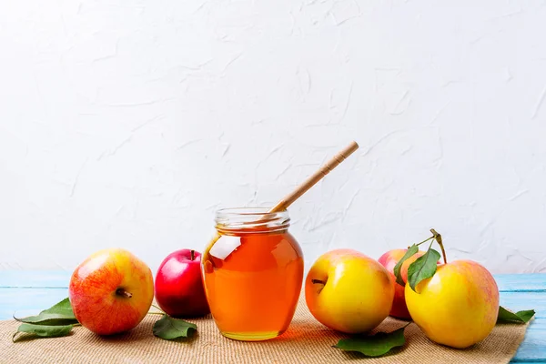 Honey jar with dipper and apples on white background