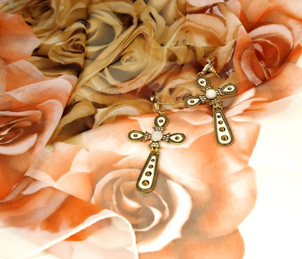 Cross earrings on beige organza kerchief covered with roses