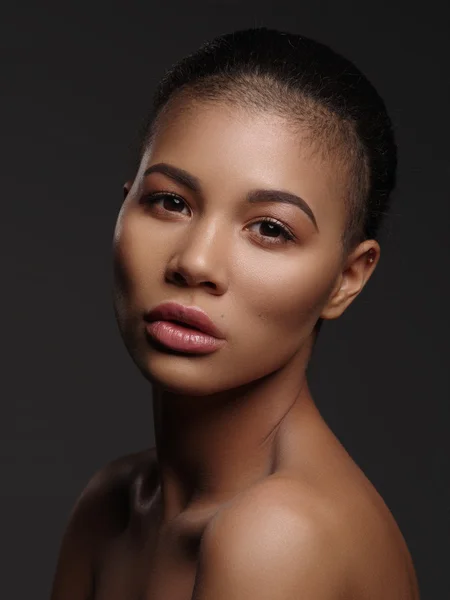 Fashion portrait of an extraordinary beautiful african american young woman with perfect smooth golden skin, full lips and shaved haircut, studio shoot, dark background