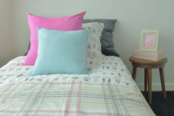 Light blue and pink pillow on sweet bedding and picture frame on bedside table