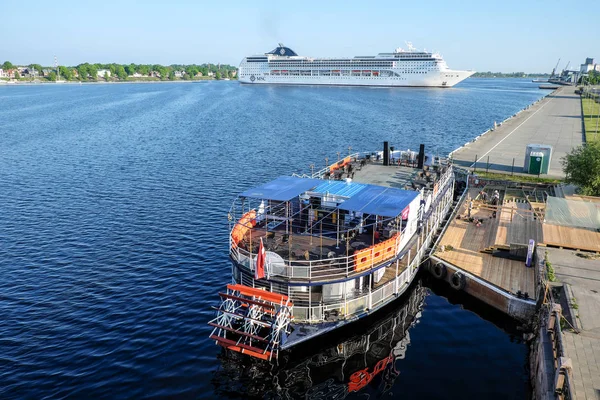 Riga, Latvia - May 21, 2016: Cruise Ship MSC Opera turning round and Touristic river boat with paddle wheel by the city embankement