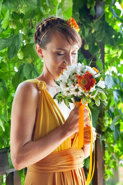 Young beautiful girl bride in a bright orange dress in the Russian wooden house. Summer bouquet in hands of the bride. Decoration of flowers in their hair hairstyle. Hippie Bride. Sunny mood.
