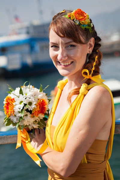 Young beautiful girl in the bright orange bride on a background of lake. Summer bouquet in hands of the bride. Decoration of flowers in their hair hairstyle. Hippie Bride on the shore of Lake Baikal.