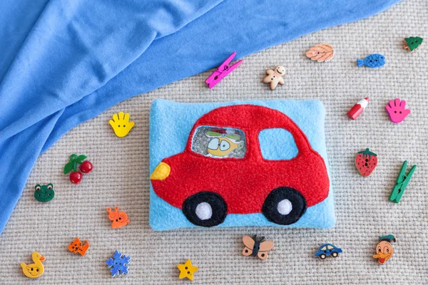 Childrens soft toy red machine of colored fleece for motor development. Bag fleece filled with plastic beads and figurines on the background of scattered toys and blue fabric. handmade toys.