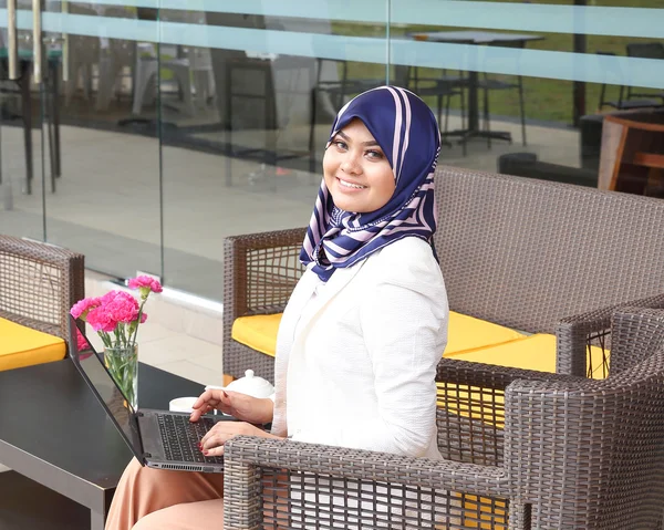 Asian Muslim woman headscarf sitting outdoor laptop smile look f