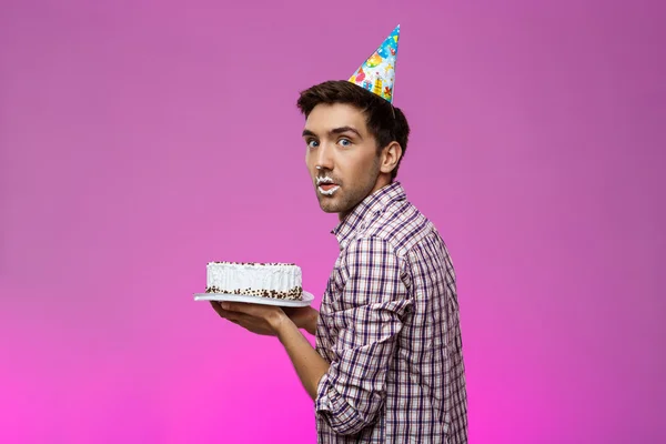 Man with cake on lips over purple background. Birthday party.