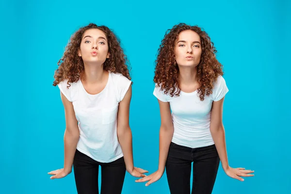 Two girls twins sending kiss, posing over blue background.