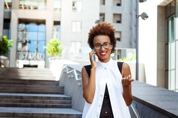 Beautiful african girl smiling speaking on phone walking down city.