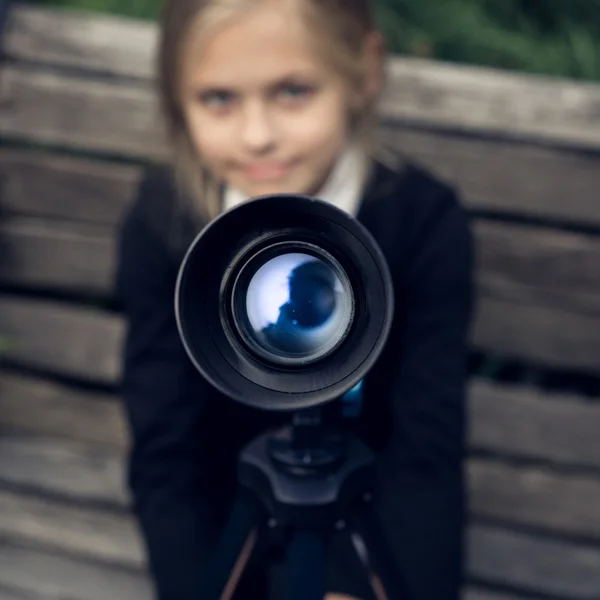 Beautiful blond girl in a school uniform in the park looking through  telescope