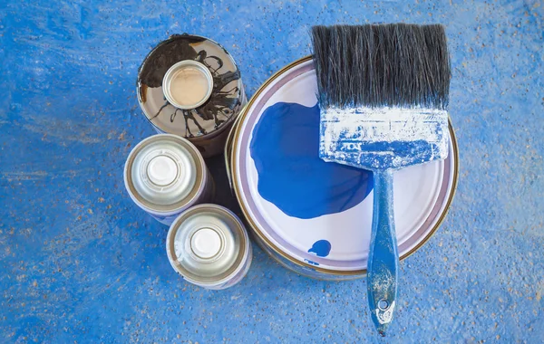 Paint cans and paint brush on the blue ground.