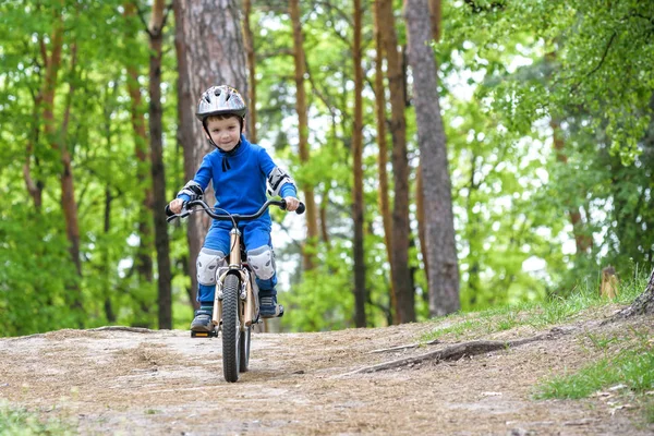 Happy funny little kid boy in colorful raincoat riding his first bike on cold day in forest. Active leisure for children outdoors.  carefree childhood concept