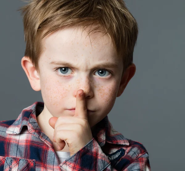 Serious young boy asking for silence with finger on lips