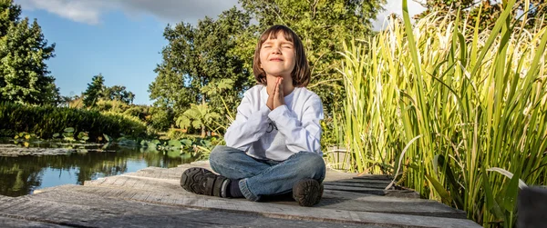 Quiet child doing yoga sitting alone, closing eyes in park