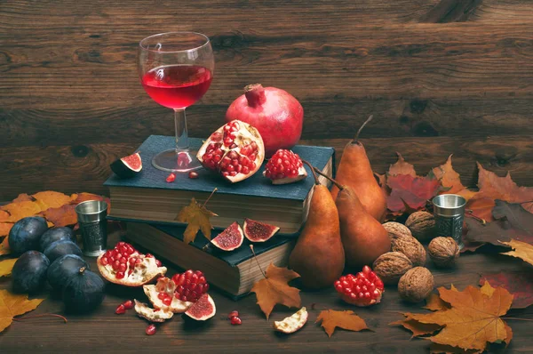 Autumn composition with a glass of red wine with pomegranate on a dark wooden background. Next autumn fruits such as figs, pears and pomegranates, and walnuts. Vegetarian, vegan concept