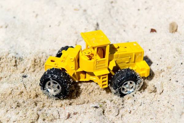 Toy tractor in the wet sand. Summer holidays at sea. Special miniature.