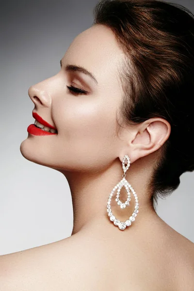 Beautiful happy woman in luxury fashion earrings. Diamond shiny jewelry with brilliants. Sexy retro style portrait. Model with glamour accessories jewelery and bright red lips makeup