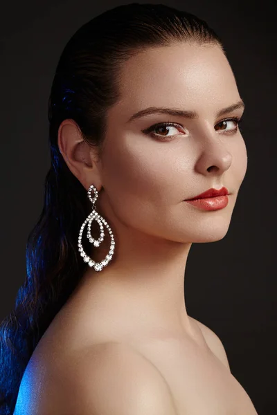 Beautiful woman in luxury fashion earrings. Diamond shiny jewelry with brilliants. Sexy retro style portrait. Model with glamour accessories jewelery, fashion makeup, clean shiny skin and wet hair