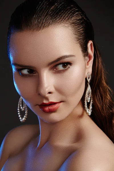 Beautiful woman in luxury fashion earrings. Diamond shiny jewelry with brilliants. Sexy retro style portrait. Model with glamour accessories jewelery, fashion makeup, clean shiny skin and wet hair